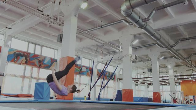 Indoor trampoline training. Flexible girl soars in the air and demonstrates a spectacular stretching. She lands on her back and jumps again. Active lifestyle, sports discipline