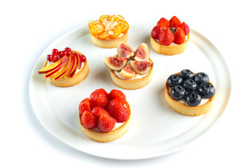 tartlets with fruits and berries in a plate on an isolated white background