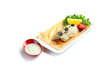baked fish fillet with tomato, lemon, herbs and sauce on an isolated white background