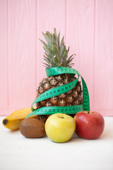 Diet weight loss breakfast concept with tape measure organic apple, orange, kiwi, grapefruit, bananas on a white background