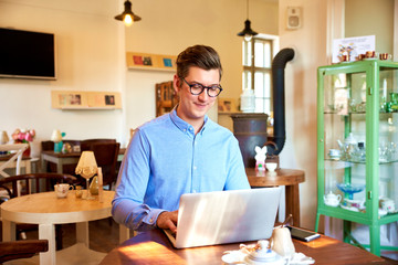 Young coffee shop owner businessman working on his laptop