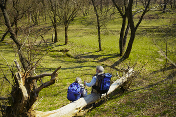 Fototapeta premium Appeasement and control. Aged family couple of man and woman in tourist outfit walking at green lawn near by trees in sunny day. Concept of tourism, healthy lifestyle, relaxation and togetherness.