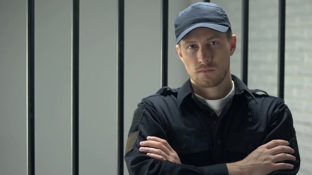 Confident prison security guard looking to camera standing near cell, profession