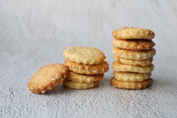 Two columns of uneven round light brown homemade cracker biscuits with sesame seeds on a grey conrete background with copy space