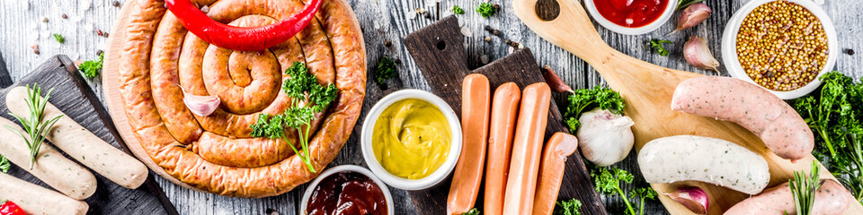 Set of various sausages ready for grilling, with different sauces, white wooden background copy space