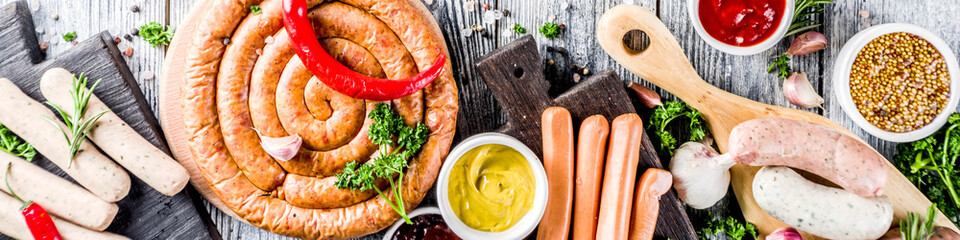 Set of various sausages ready for grilling, with different sauces, white wooden background copy space