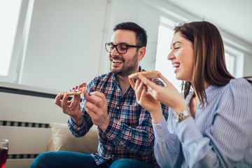 Beautiful young couple eating pizza,talking and smiling at home.