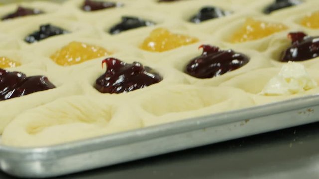 Adding Fruit And Cream Cheese Filling To Traditional Fruit Kolache On Baking Tray. Woman adds fruit and cream cheese filling to fruit kolaches on a baking tray.