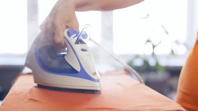 Woman ironing an orange shirt with a steam iron