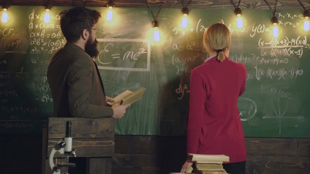 Teacher and female student solve mathematical formulas and record them with chalk on a board. Classmate Educate Friend Knowledge Lesson Concept. Education, school, college and university concept.