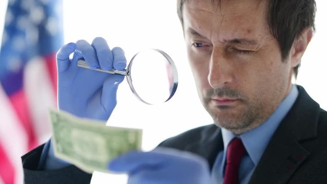 American secret service agent analyzing suspicious counterfeit dollar bill, conceptual footage