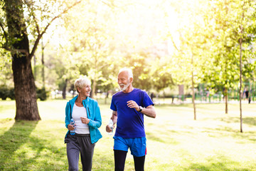 Happy senior couple jogging outdoors in park.