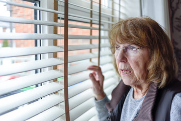 Elderly Lady Looking Through Window Blinds at Home.