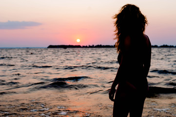 back view of woman figure in swimsuit looking at amazing sunrise near sea on beach