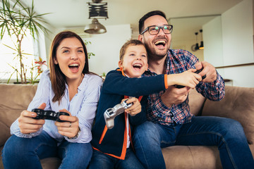 Happy family sitting on a sofa and playing video games and eating pizza