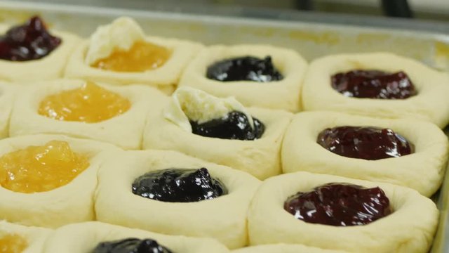 close up of woman adding fruit and cream cheese filling to kolache dough.  Woman adds cream cheese filling to fruit kolaches.