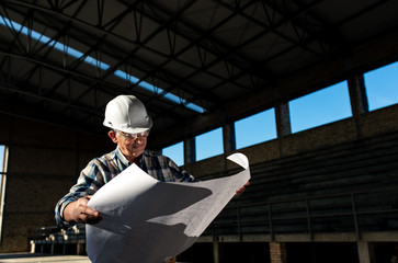 Senior construction manager with blueprint controlling building site.	