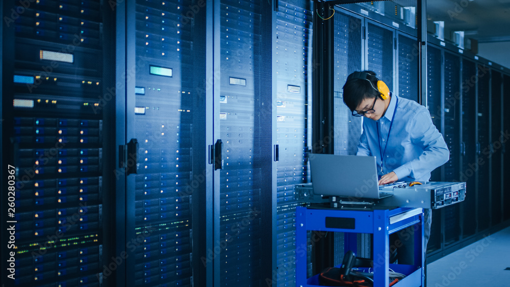 Poster In the Modern Data Center: IT Technician Wearing Protective Headphones Working with Server Racks, on a Pushcart Installing New Hardware. Engineer Doing Maintenance and Diagnostics of the Database.