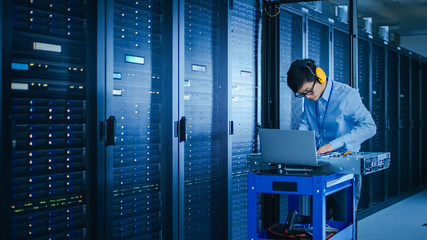 In the Modern Data Center: IT Technician Wearing Protective Headphones Working with Server Racks, on a Pushcart Installing New Hardware. Engineer Doing Maintenance and Diagnostics of the Database.