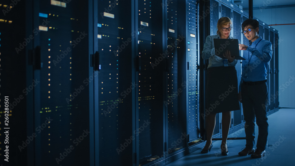 Poster In the Modern Data Center: Engineer and IT Specialist Work with Server Racks, Talking, Doing System Maintenance Check with Laptop Computer. Concept of Diagnostics of the Database, Cybersecurity Check