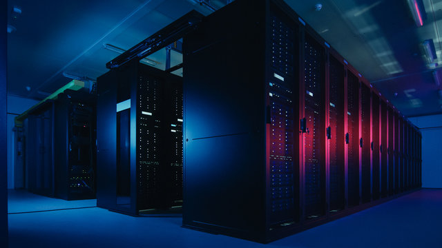 Shot of Data Center With Multiple Rows of Fully Operational Server Racks. Modern Telecommunications, Cloud Computing, Artificial Intelligence, Database. Shot in Dark with Neon Blue, Pink Lights.