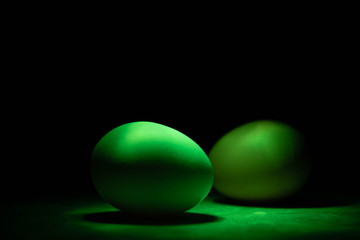 Unusual green chicken eggs in green light on black background
