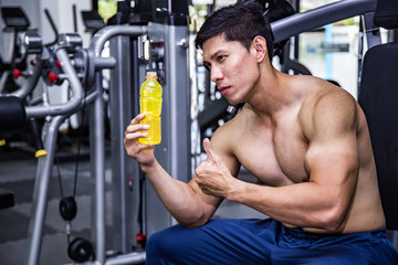 Fototapeta na wymiar Asian fit man with energy drink relaxing and drinking in the gym. Sport and fittness concept.And Asian handsome muscles are tired, so drink Electrolyte drink.