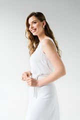 cheerful girl in dress smiling while standing on white