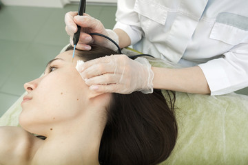 Fototapeta premium Medical treatment removal of birthmark from female patient's face. Female dermatologist surgeon using a professional electrocautery for removing mole. Radio wave electrocoagulation remove method