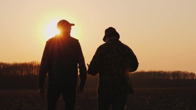 Farmers father and son walk across the field at sunset, chatting