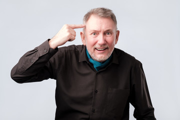 senior man smiling pointing to head with one finger, great idea or thought