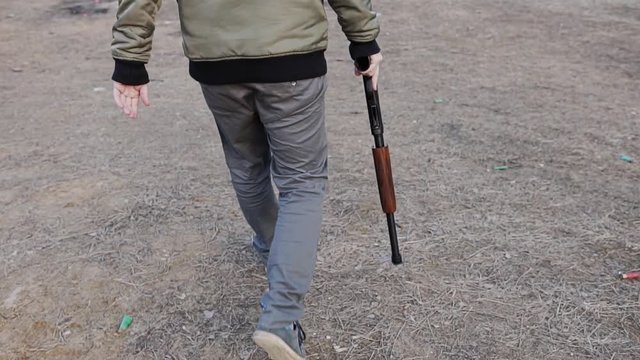 The guy with the shotgun in his right hand goes to the shooting range. The camera is in motion. The camera follows the shooter. Slow playback