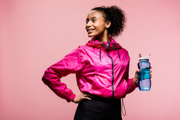 beautiful smiling african american sportswoman with sport bottle isolated on pink © LIGHTFIELD STUDIOS