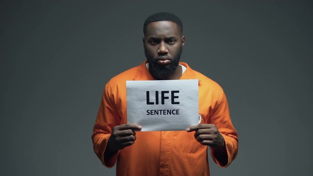 Afro-american imprisoned male holding Life sentence sign, looking to camera