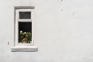 A small window in an old shabby white wall