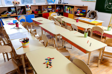 Room in elementary school, interior with light wooden furniture and learning aids on the walls. Pencils on the tables. No one, the children went for a walk