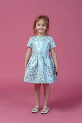 Little girl in elegant blue dress. Girl posing on a pink background. Fashion photo.