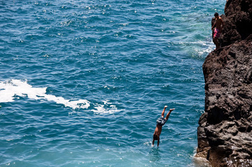 Junge springt von einer Klippe ins Meer