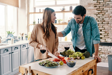 Doing everything together. Beautiful young couple cooking dinner and drinking wine while standing in the kitchen at home