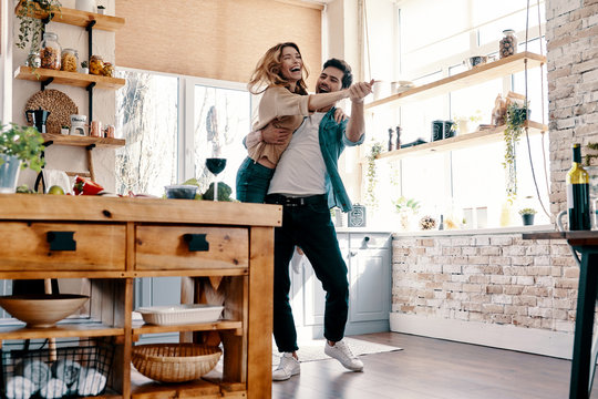 Playful. Full length of beautiful young couple in casual clothing dancing and smiling while standing in the kitchen at home