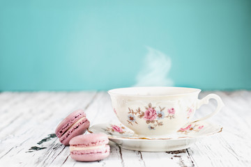 Antique Bavaria Winterling footed tea cup from the 1950s' with pink macarons on a rustic white table against a teal background..