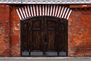 Fototapeta premium Ancient wooden entrance door in a brick wall of old and new bricks of different sizes