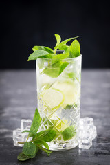 Cold drink with lime, mint and soda isolated on textured gray table and black background