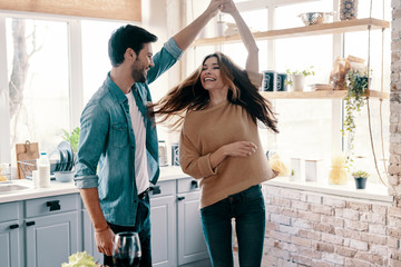 In love. Beautiful young couple in casual clothing dancing and smiling while standing in the kitchen at home