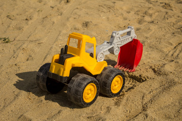 Yellow excavator toy in sand, on the beach. Boy's toys concept - Image