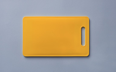 Colored yellow plastic cutting board on blue background, top view.