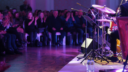 A man in costume playing drums at the jazz concert. The audience clapping their hands
