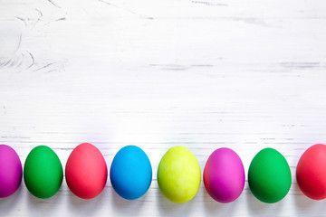 Row colorful Easter eggs on white wooden background