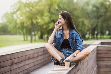 Young woman talking on phone in a park. Beautiful student girl using smartphone in a city