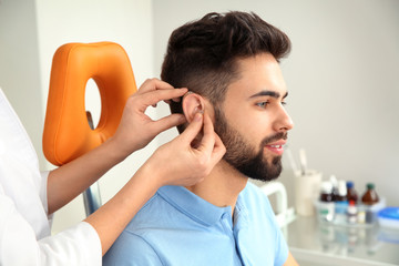 Otolaryngologist putting hearing aid in patient's ear at clinic